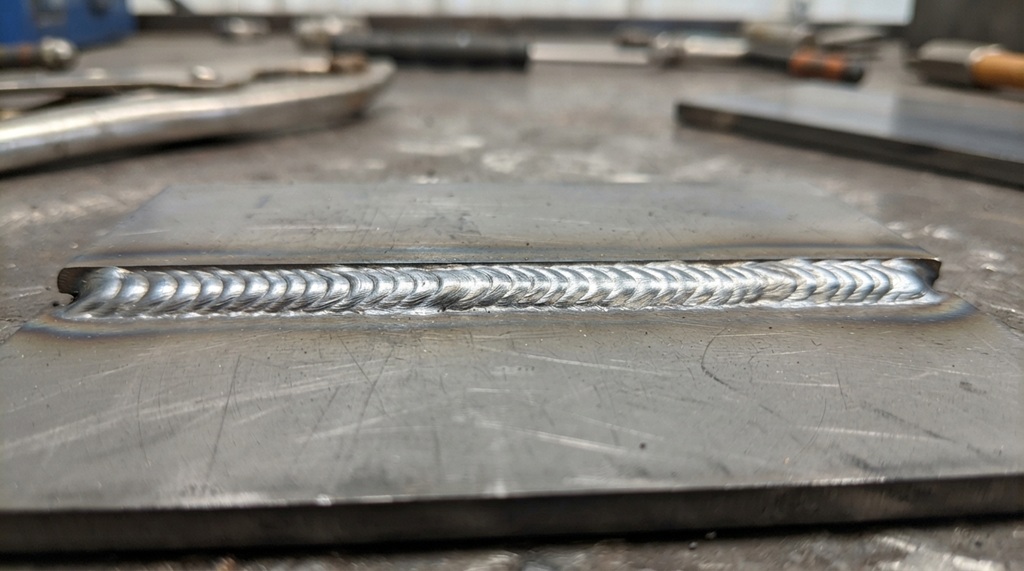 Clean steel test weld bead with minimal spatter on metal plate.