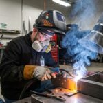 Male welder wearing a protective respirator while extracting metal fumes.